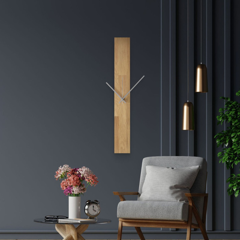 Moderné nástenné hodiny, nalepené na bielej stene, s jednoduchými čiernymi ručičkami.