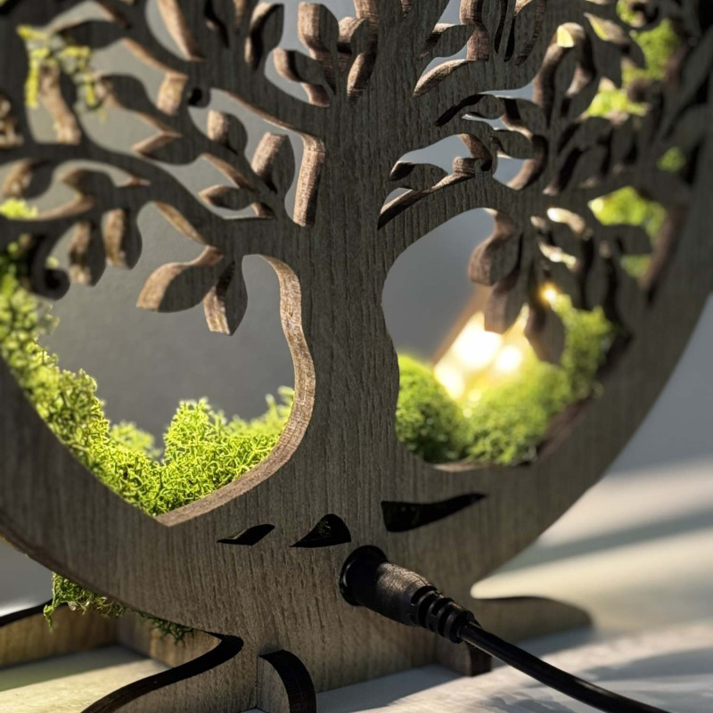 Detailný pohľad na podsvietený drevený Strom života obklopený machom.